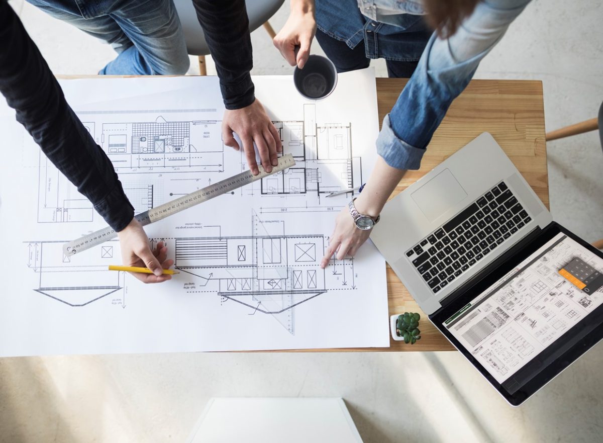 Arquitectos trabajando en planos de diseño de viviendas con herramientas y laptop