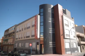 edificio moderno en esquina con fachada combinada en tonos beige, gris y rojo, con ventanas y cristalera vertical