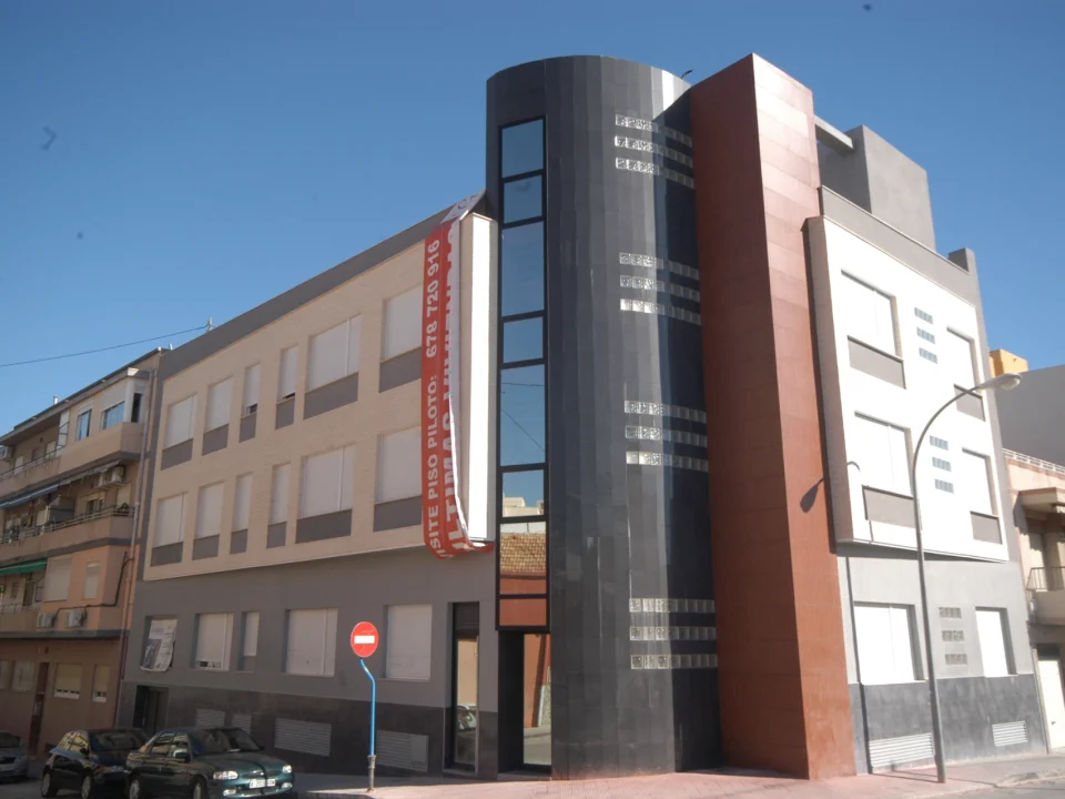 edificio moderno en esquina con fachada combinada en tonos beige, gris y rojo, con ventanas y cristalera vertical