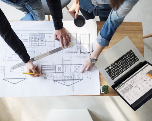 Arquitectos trabajando en planos de diseño de viviendas con herramientas y laptop