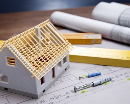 modelo de casa en construcción sobre planos arquitectónicos con herramientas de medición, concepto de diseño y planificación de viviendas." Este texto es descriptivo y contiene palabras clave relevantes para el sector de arquitectura, construcción y diseño de viviendas, ayudando a posicionar mejor la imagen en buscadores
